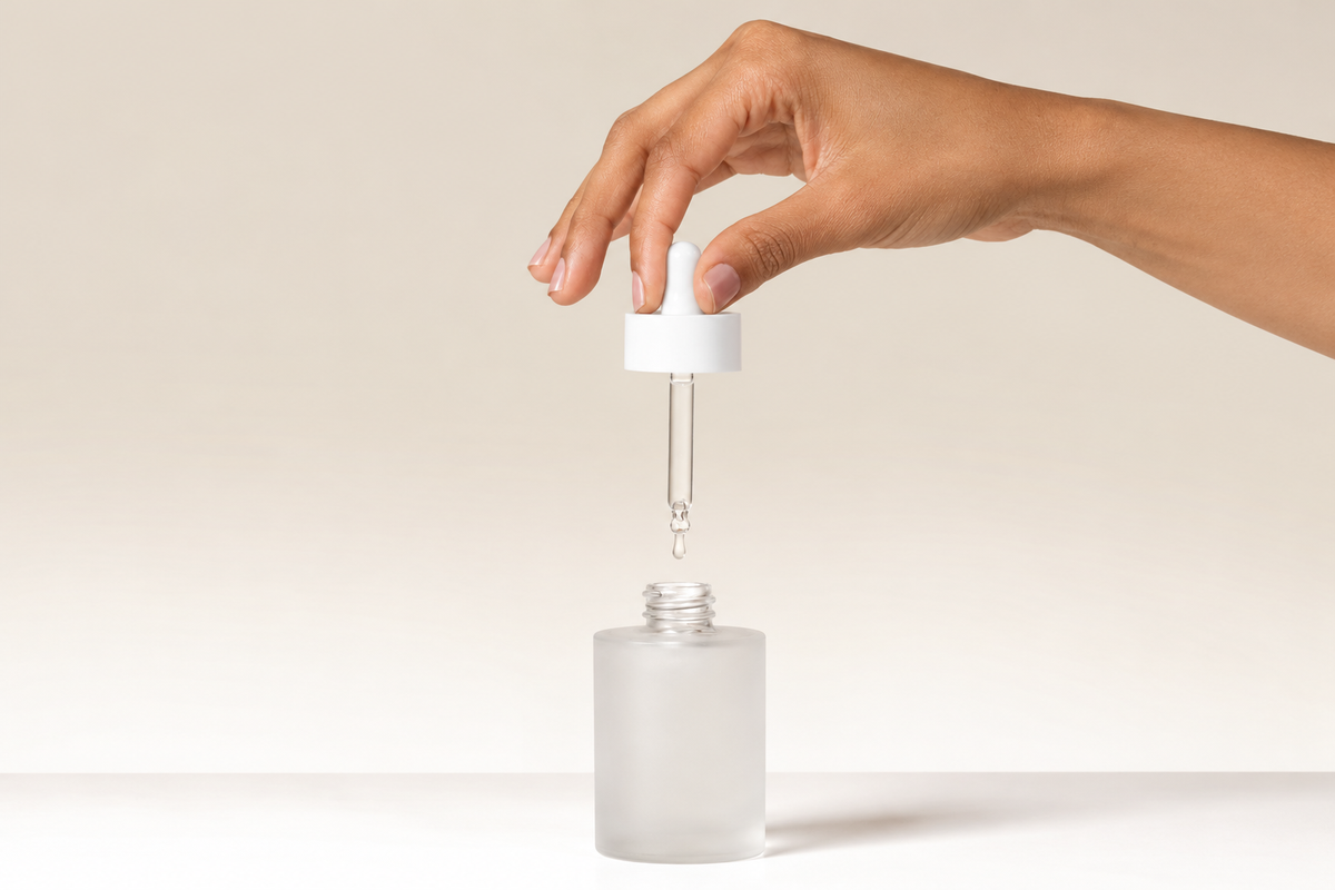 Hand holding a face serum dropper above a frosted glass bottle, illustrating skincare for pigmentation, dark spots and uneven skin tone.
